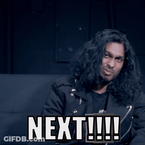 A Man With Long Hair Is Sitting Next To A Sign That Says Next GIF
