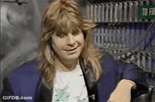 A Man With Long Hair Is Sitting On A Couch Smiling . GIF