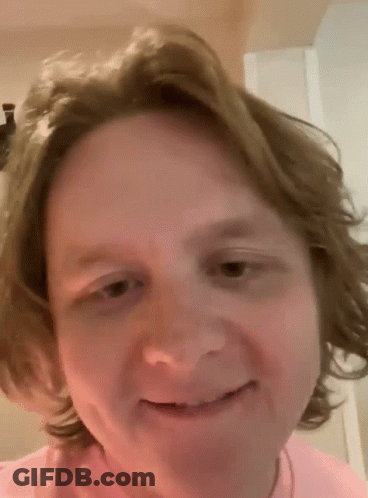 A Man With Long Hair Is Smiling And Wearing A Pink Shirt GIF