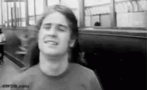 A Man With Long Hair Is Smiling In A Black And White Photo While Sitting In A Restaurant . GIF