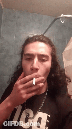 A Man With Long Hair Is Smoking A Cigarette While Wearing A Black Shirt That Says T2u GIF