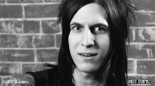 A Man With Long Hair Is Standing In Front Of A Brick Wall And Smiling . GIF