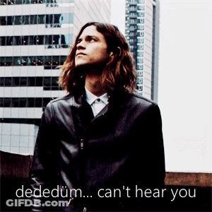 A Man With Long Hair Is Standing In Front Of A Building With The Words Dededum Can 'T Hear You Written Below Him GIF