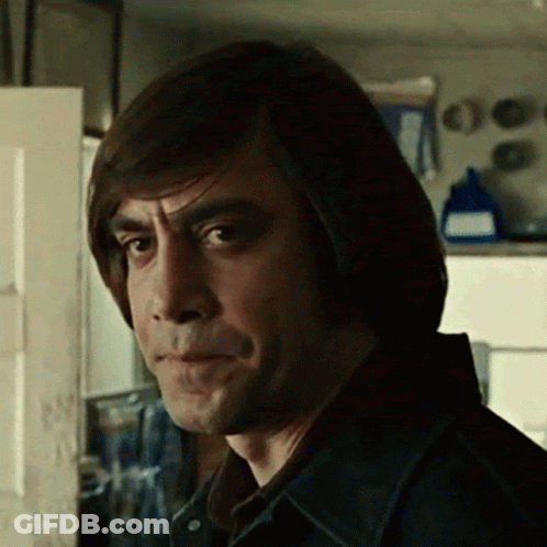 A Man With Long Hair Is Standing In Front Of A Door And Making A Funny Face . GIF