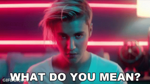 A Man With Long Hair Is Standing In Front Of A Neon Sign And Says What Do You Mean . GIF