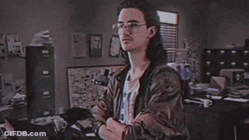 A Man With Long Hair Is Standing In Front Of A Sign That Says Hackerman GIF