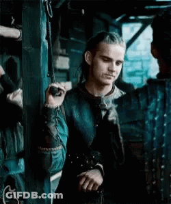 A Man With Long Hair Is Standing Next To A Wall Holding A Rope . GIF