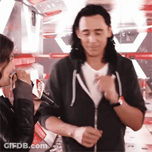 A Man With Long Hair Is Standing Next To A Woman Holding A Microphone And Talking To Her . GIF