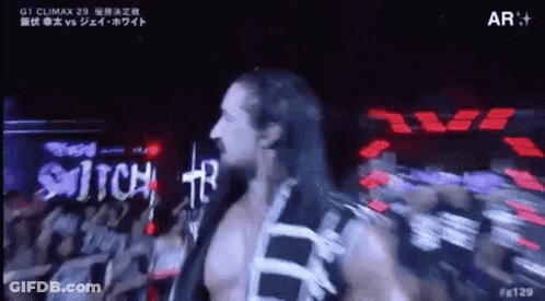 A Man With Long Hair Is Walking On A Stage In Front Of A Crowd Of People . GIF