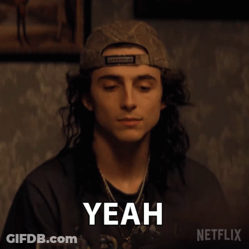 A Man With Long Hair Is Wearing A Baseball Cap And Making A Yeah Gesture . GIF