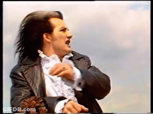 A Man With Long Hair Is Wearing A Black Leather Jacket And White Shirt GIF