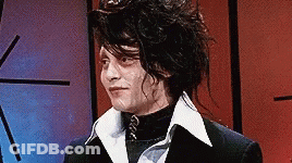 A Man With Long Hair Is Wearing A Black Suit And A White Collar . GIF
