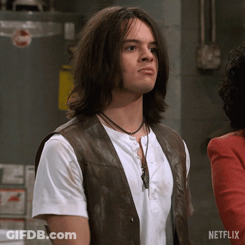 A Man With Long Hair Is Wearing A Brown Vest And A White Shirt With A Netflix Logo On The Bottom GIF