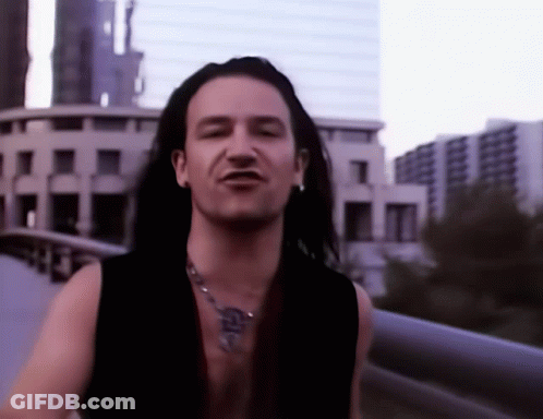 A Man With Long Hair Is Wearing A Necklace With A Cross On It GIF