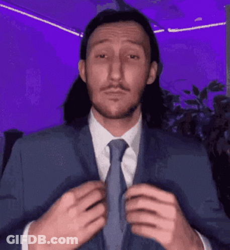 A Man With Long Hair Is Wearing A Suit And Tie GIF