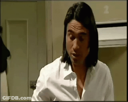 A Man With Long Hair Is Wearing A White Shirt And Looking Down . GIF