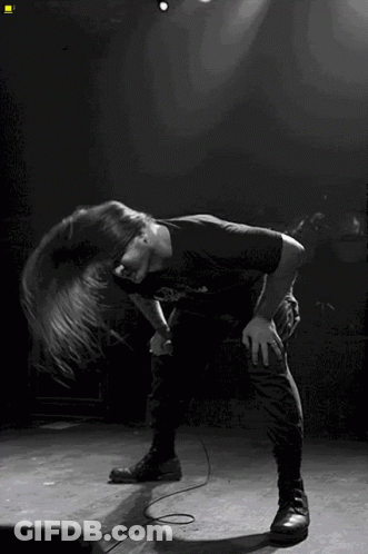 A Man With Long Hair Singing Into A Microphone On Stage GIF