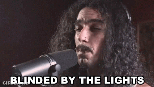 A Man With Long Hair Singing Into A Microphone With The Words Blinded By The Lights Below Him GIF