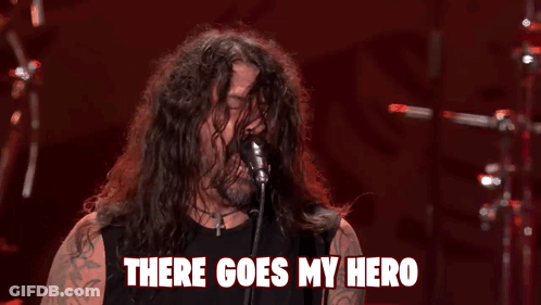 A Man With Long Hair Singing Into A Microphone With The Words " There Goes My Hero " Above Him GIF