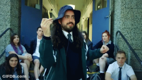 A Man With Long Hair Wearing A Blue Hat Stands In Front Of A Group Of Students GIF