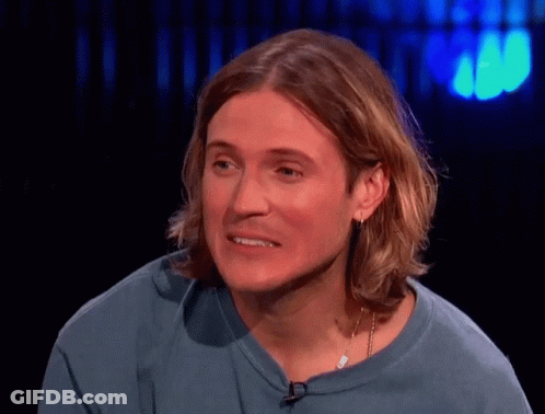 A Man With Long Hair Wearing A Blue Shirt And Earrings GIF