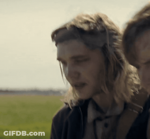 A Man With Long Hair Wearing Headphones Stands Next To A Woman In A Field GIF