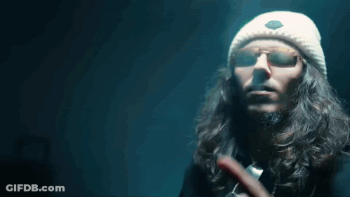 A Man With Long Hair Wearing Sunglasses And A White Hat Points To The Word My GIF