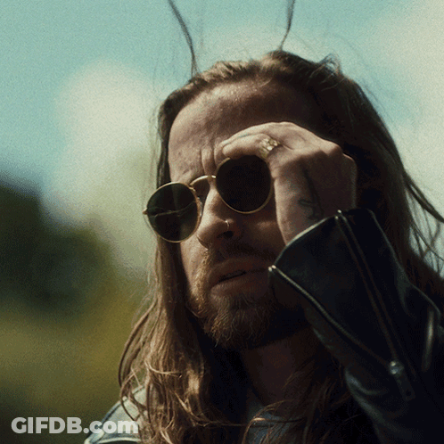 A Man With Long Hair Wearing Sunglasses Has A Tattoo On His Arm GIF