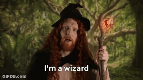 A Man With Long Red Hair Is Dressed As A Wizard And Holding A Wand . GIF