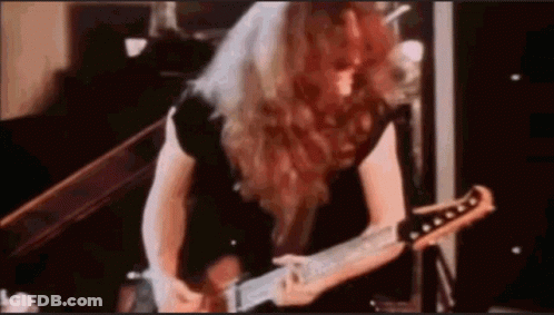 A Man With Long Red Hair Is Playing A Guitar In A Room . GIF