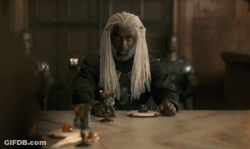 A Man With Long White Dreadlocks Sits At A Table GIF