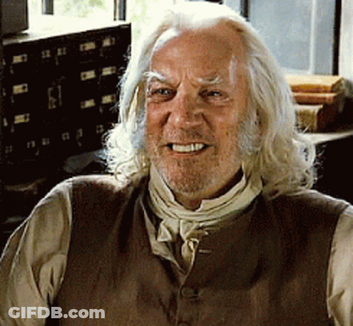 A Man With Long White Hair And A Beard Wears A Brown Vest GIF