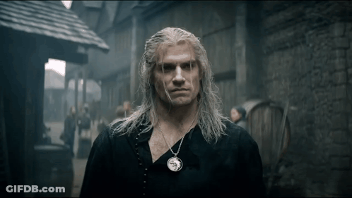 A Man With Long White Hair And A Necklace On His Neck Is Standing In Front Of A Brick Building . GIF