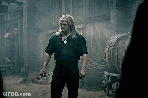 A Man With Long White Hair Is Holding A Sword In Front Of A Building And Barrels . GIF