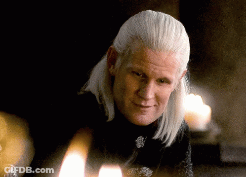 A Man With Long White Hair Is Sitting In Front Of A Candle GIF