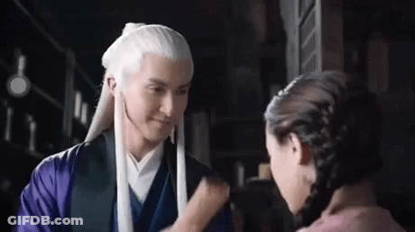 A Man With Long White Hair Is Standing Next To A Woman In A Purple Dress . GIF