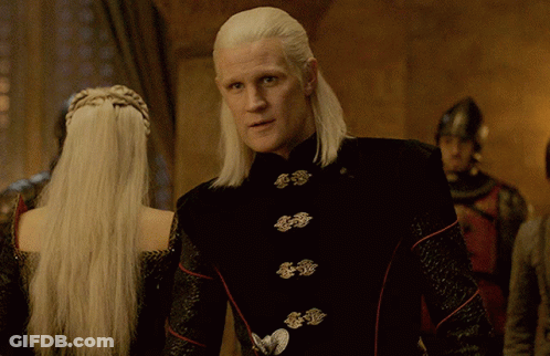 A Man With Long White Hair Is Standing Next To A Woman GIF
