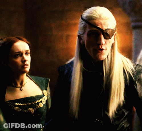 A Man With Long White Hair Wearing A Black Eye Patch Stands Next To A Woman GIF