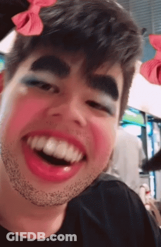 A Man With Makeup On His Face And A Bow On His Head Is Smiling GIF