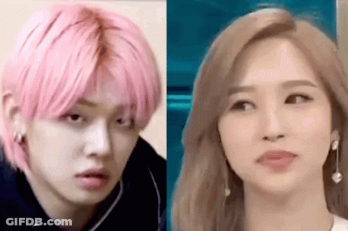 A Man With Pink Hair And A Woman With Blonde Hair Are Standing Next To Each Other And Looking At Each Other . GIF