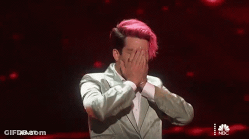 A Man With Pink Hair Is Covering His Face With His Hands While Wearing A Suit . GIF