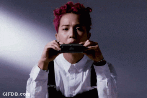 A Man With Pink Hair Is Holding A Black Object In Front Of His Mouth GIF