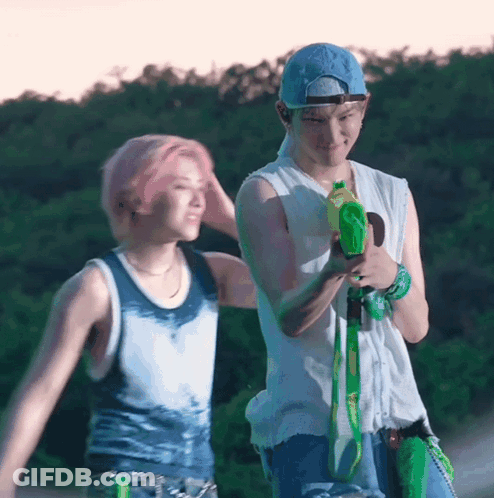 A Man With Pink Hair Is Holding A Water Gun Next To Another Man . GIF