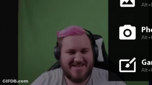 A Man With Pink Hair Is Sitting In Front Of A Green Screen . GIF