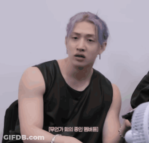A Man With Purple Hair Is Wearing A Black Tank Top And Sitting Next To A Fan GIF