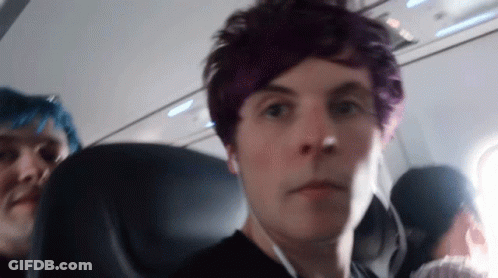 A Man With Purple Hair Looks At The Camera While Sitting On An Airplane GIF