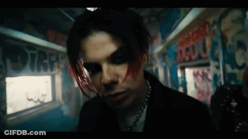A Man With Red Hair And Black Makeup Is Standing In A Room With Graffiti On The Wall . GIF