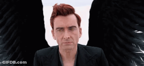 A Man With Red Hair And Black Wings Is Sitting In Front Of A White Wall . GIF