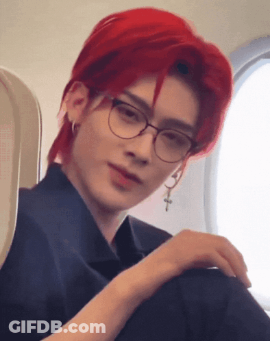 A Man With Red Hair And Glasses Is Sitting On A Plane GIF