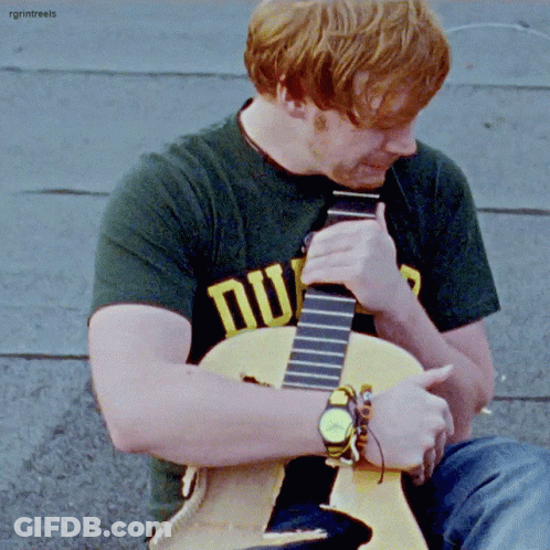 A Man With Red Hair Is Playing A Guitar And Wearing A Shirt That Says Nu GIF